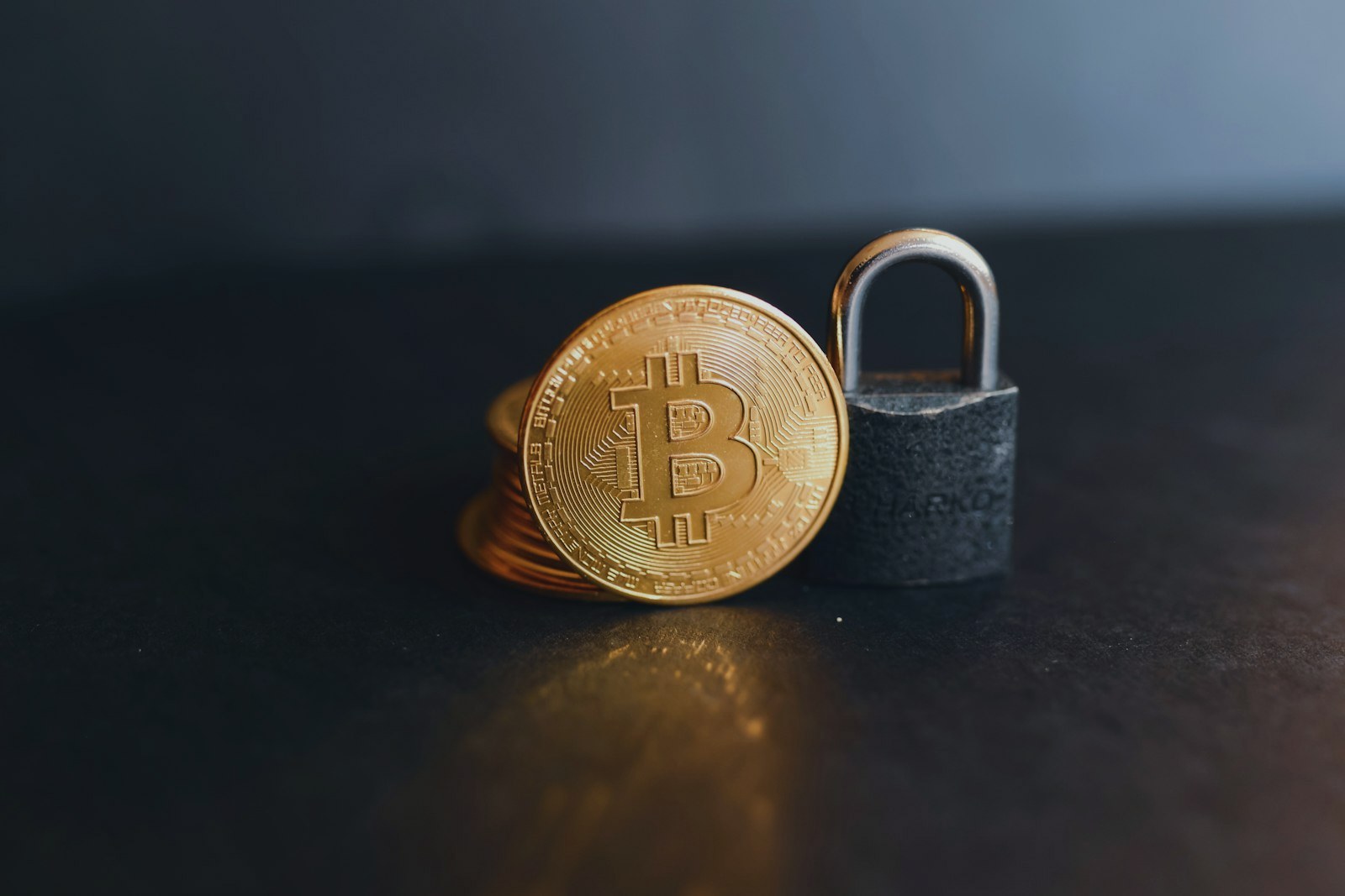 Moeda de bitcoin ao lado de um cadeado em fundo escuro